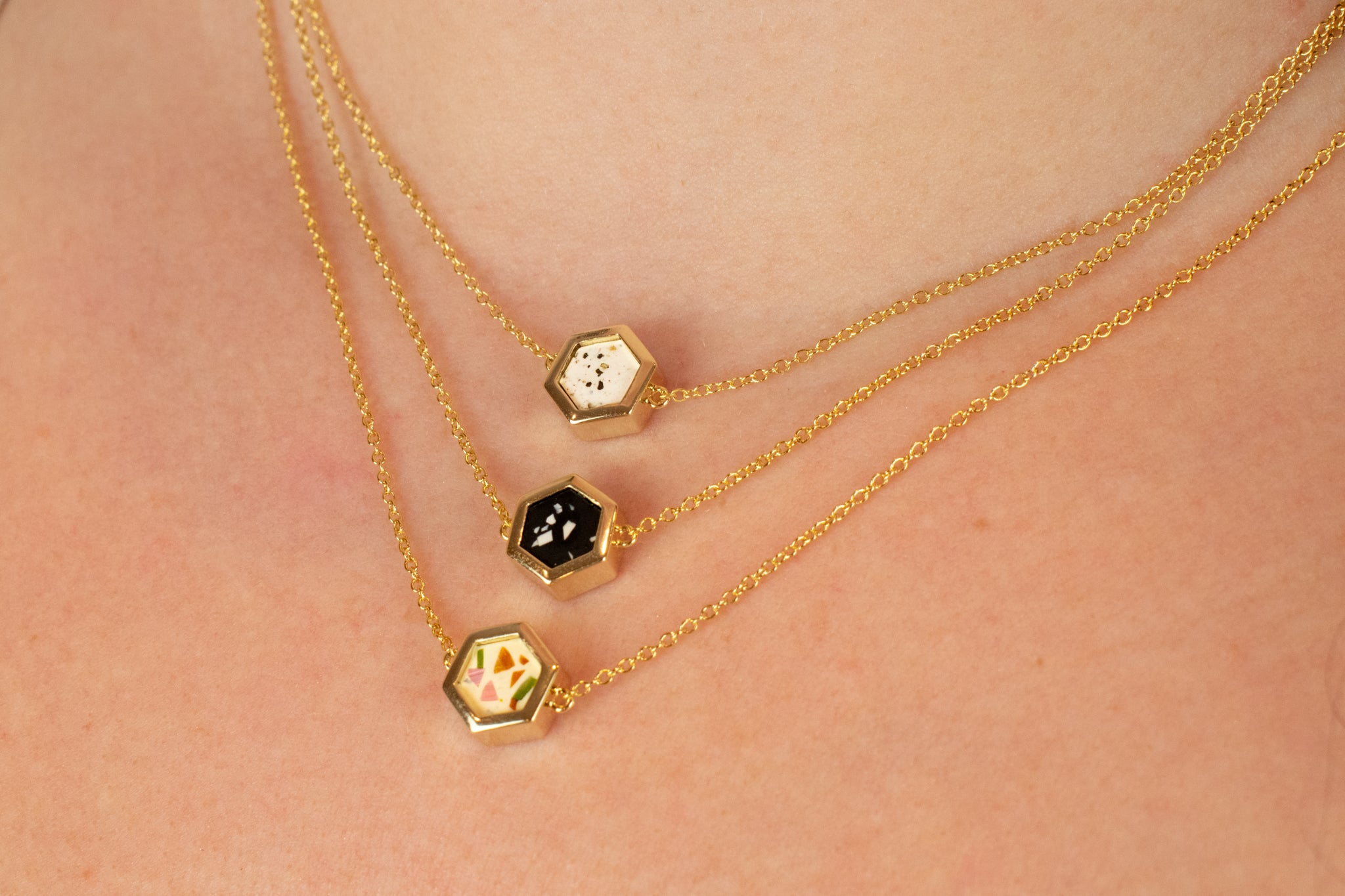 detailed close up of three adjustable gold chain necklaces all in terazo style : white speckled stone, black terrazzo with chips of white, and rainbow terrazzo