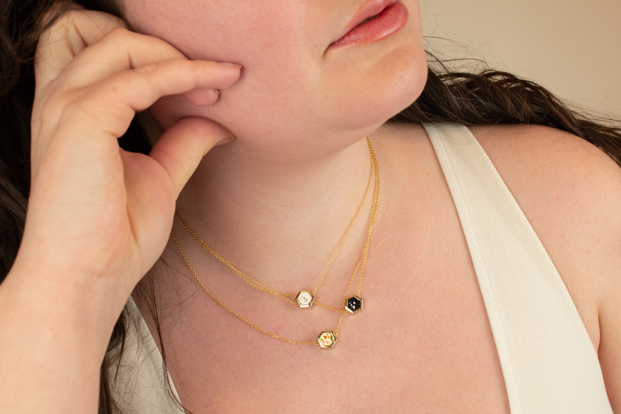 close in of model wearing three hexagon delicate chain necklaces criss crossed at different lengths