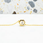 gold hexagon necklace with speckled stone displayed on white surface with stone terrazzo background