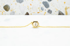 gold hexagon necklace with speckled stone displayed on white surface with stone terrazzo background