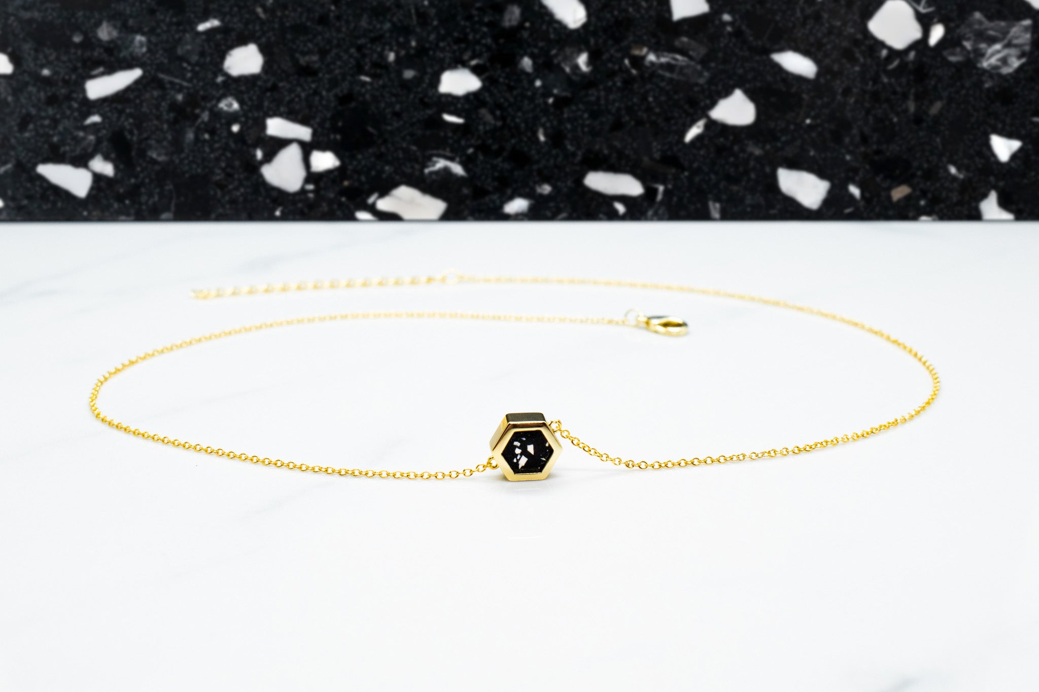 everyday gold and black statement necklace laid out in a circle displayed on white surface with black terrazzo backdrop