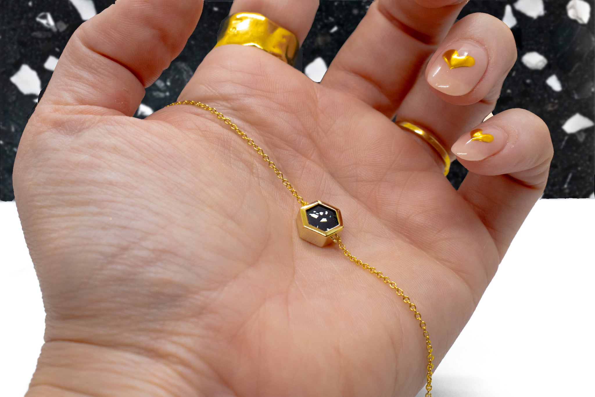 manicured hand in front of black terrazzo background holding gold plated adjustable cable chain necklace in black terazzo