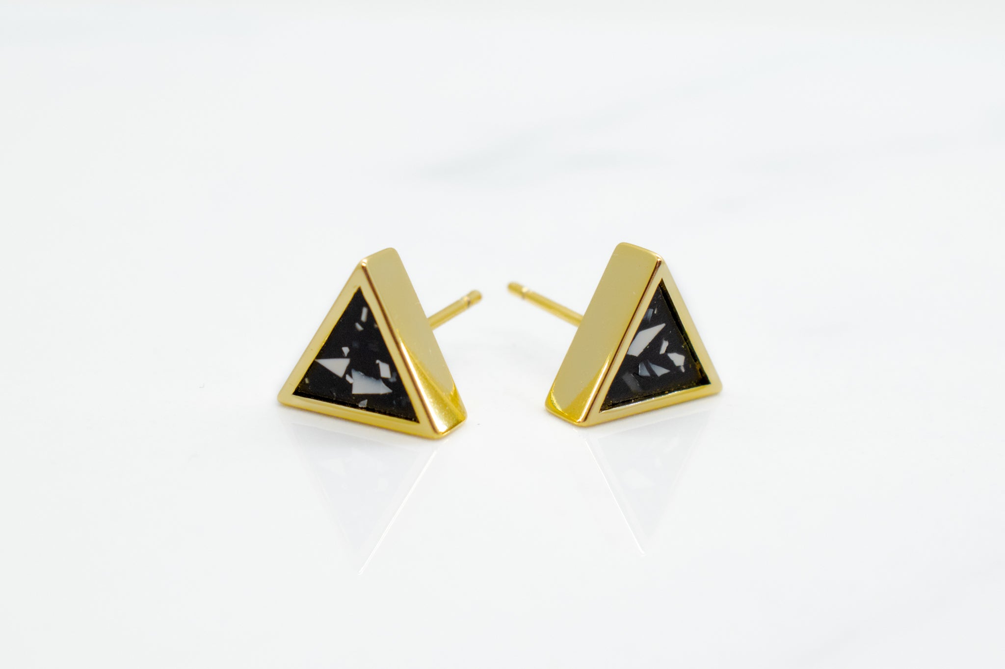 close up shot of gold triangle stud earrings with matte black clay and angular chips of white clay photographed on marble