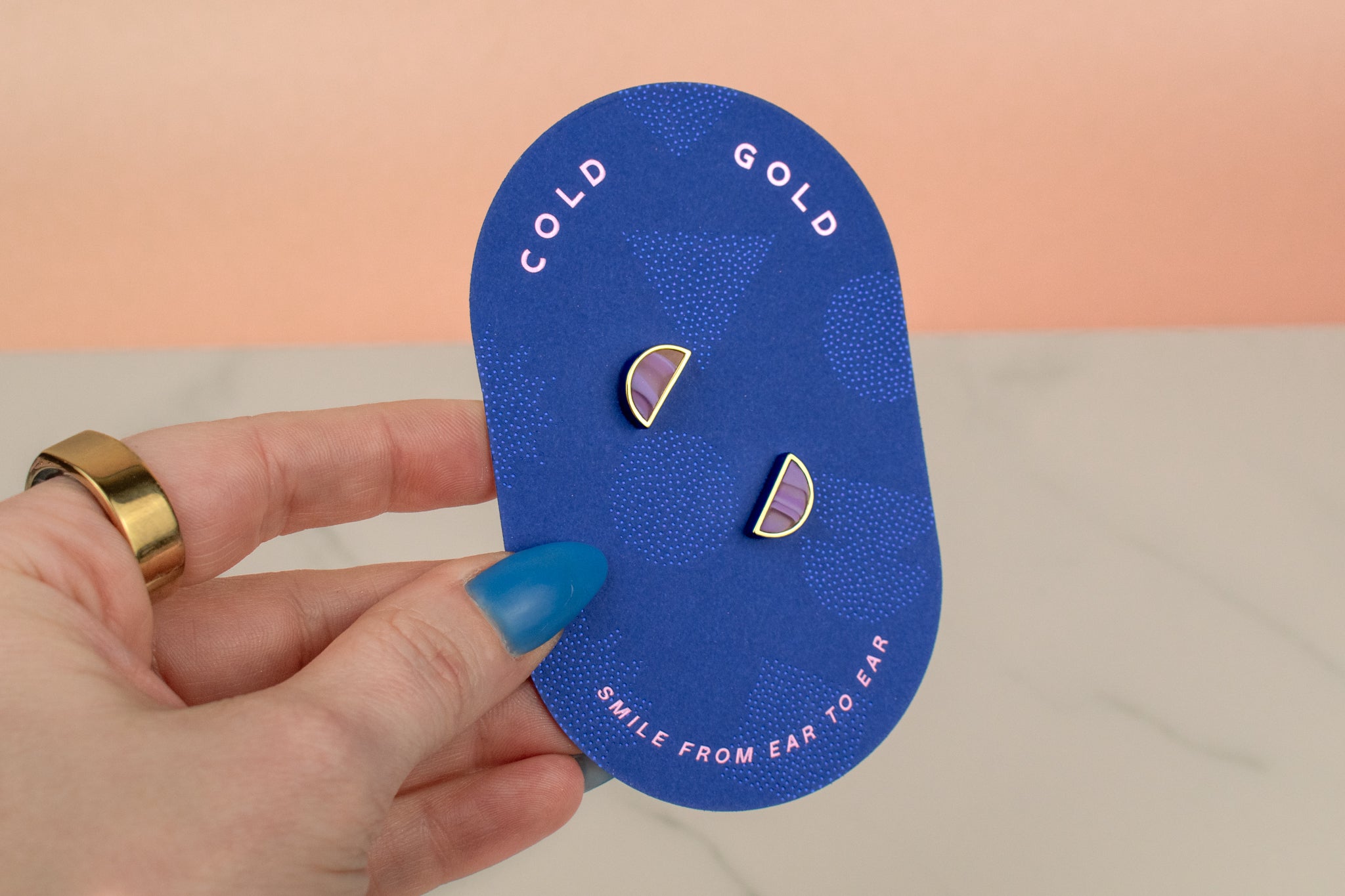 a hand holding a geometric card showing a pair of marble pastel purple half moon earring stud set