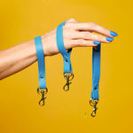A hand with bright blue fingernails displays three Matisse blue real leather wristlets with gold key rings and clasps.