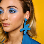 close up of woman wearing oversized leather cutout earrings in matisse blue.