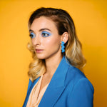 woman with blue makeup and blonde hair wearing matisse blue cutout leather statement ear rings in zig zag shape.