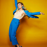 woman doing a dance pose in a blue suit wearing oversized cutout matisse earrings in blue leather.