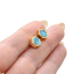 hand holding a pair of modern and minimal stud earrings in aqua crystal clay and gold
