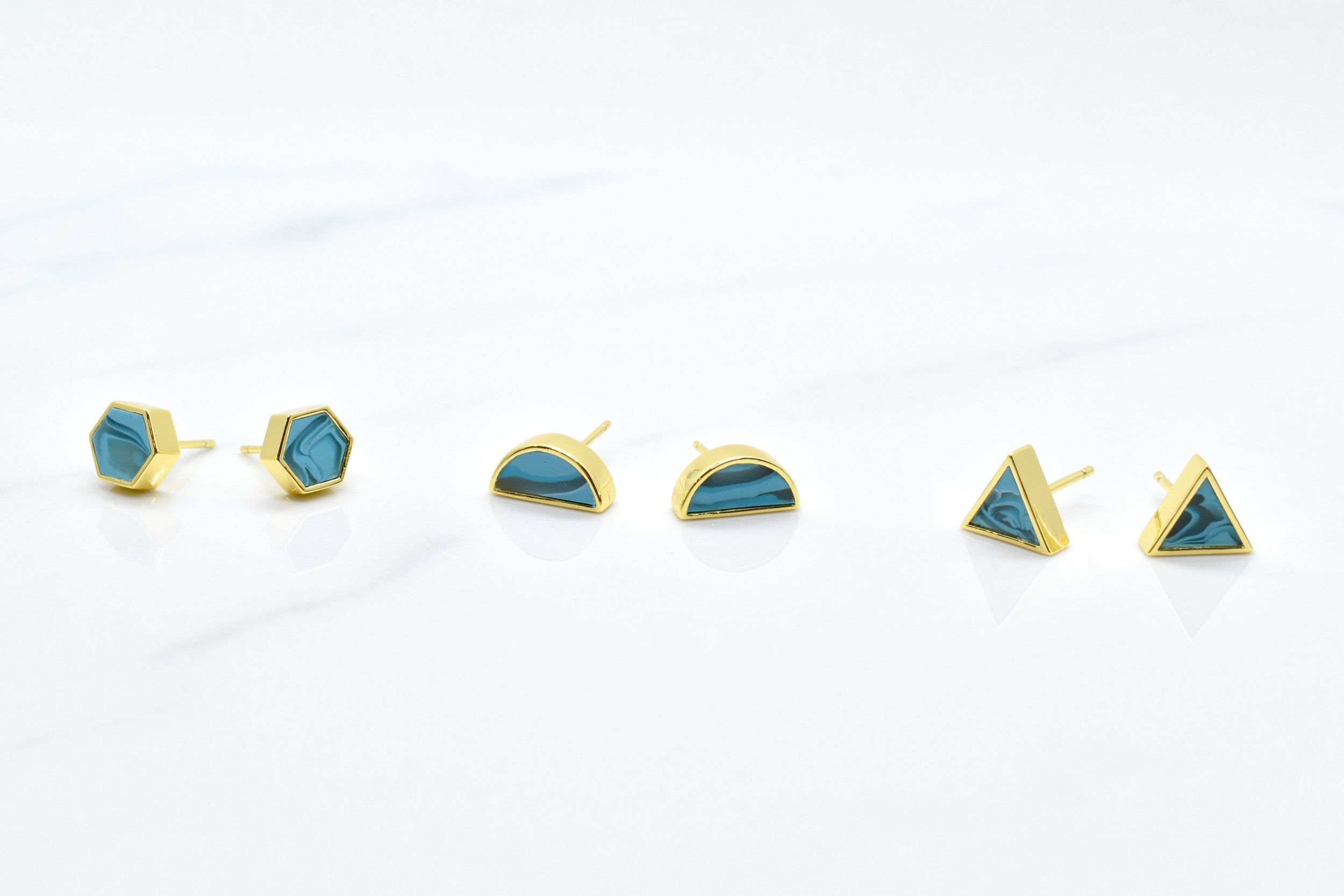 three pairs of geometric earrings shown on a white background, geometric stud set in 14k gold plated sterling silver and aqua marbled clay