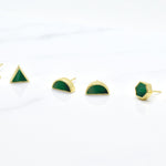 a set of three pairs of gold geometric stud earrings. One set of triangle studs, one set of gold hexagon earrings and one set of half moon stud earrings, all in emerald gemstone that's been marble