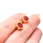 hand holding a pair of studs with 24k gold hexagons and ruby garnet gemstone modern studs against white background
