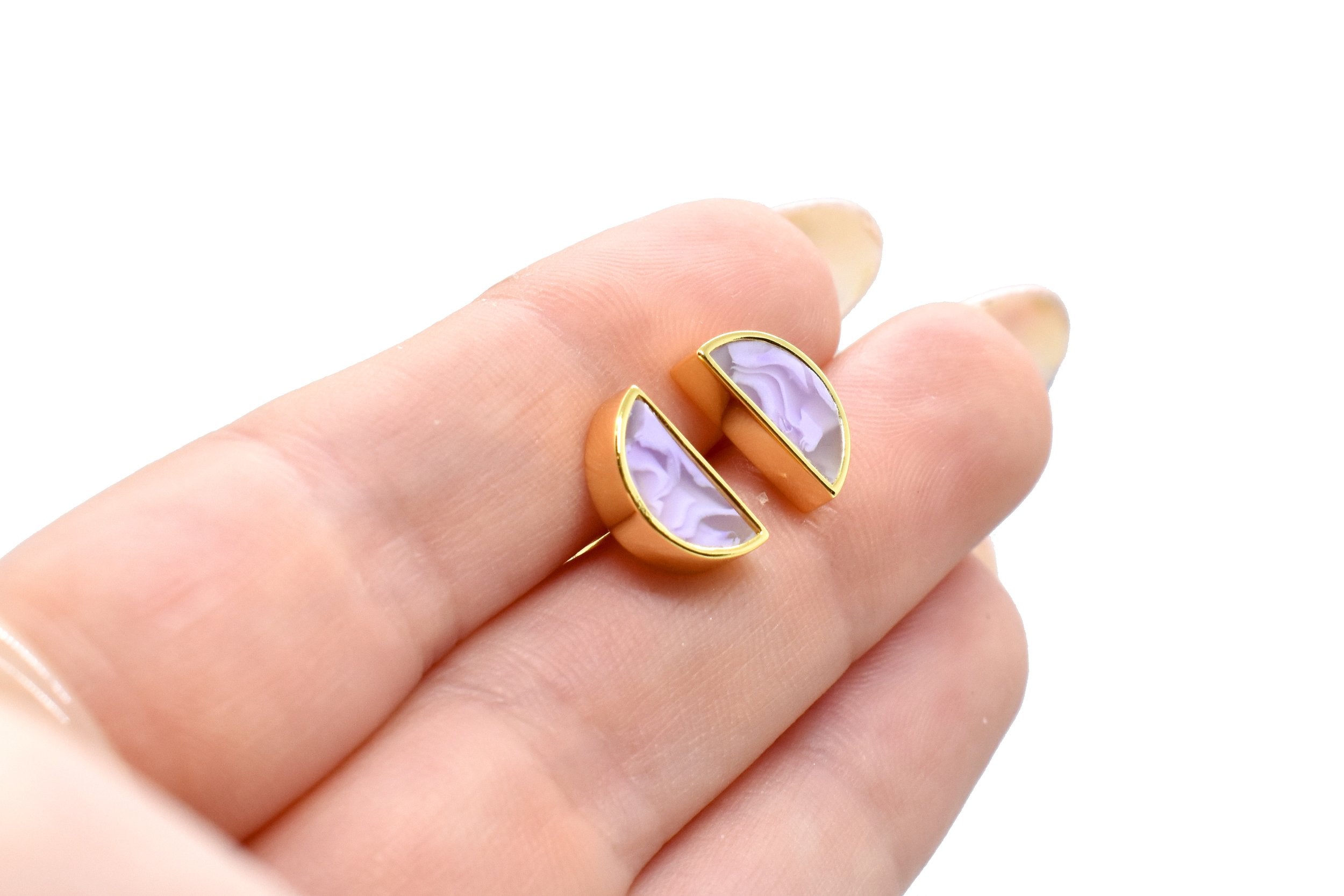 hand holding a pair of celestial gold stud earrings in amethyst marble