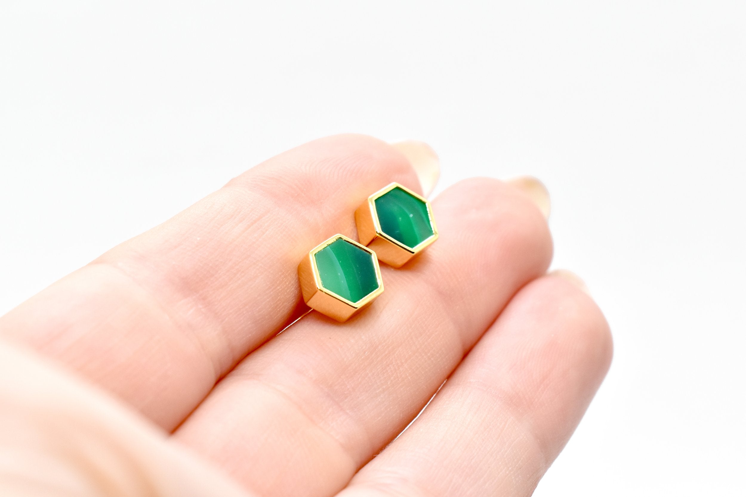 hands holding gold hexagon stud earrings with striped jade gemstone texture and 14k gold hexagon shape against a white background