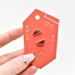 hand holding red and gold packaging card with geometric half moon stud earrings in ruby gemstone red clay