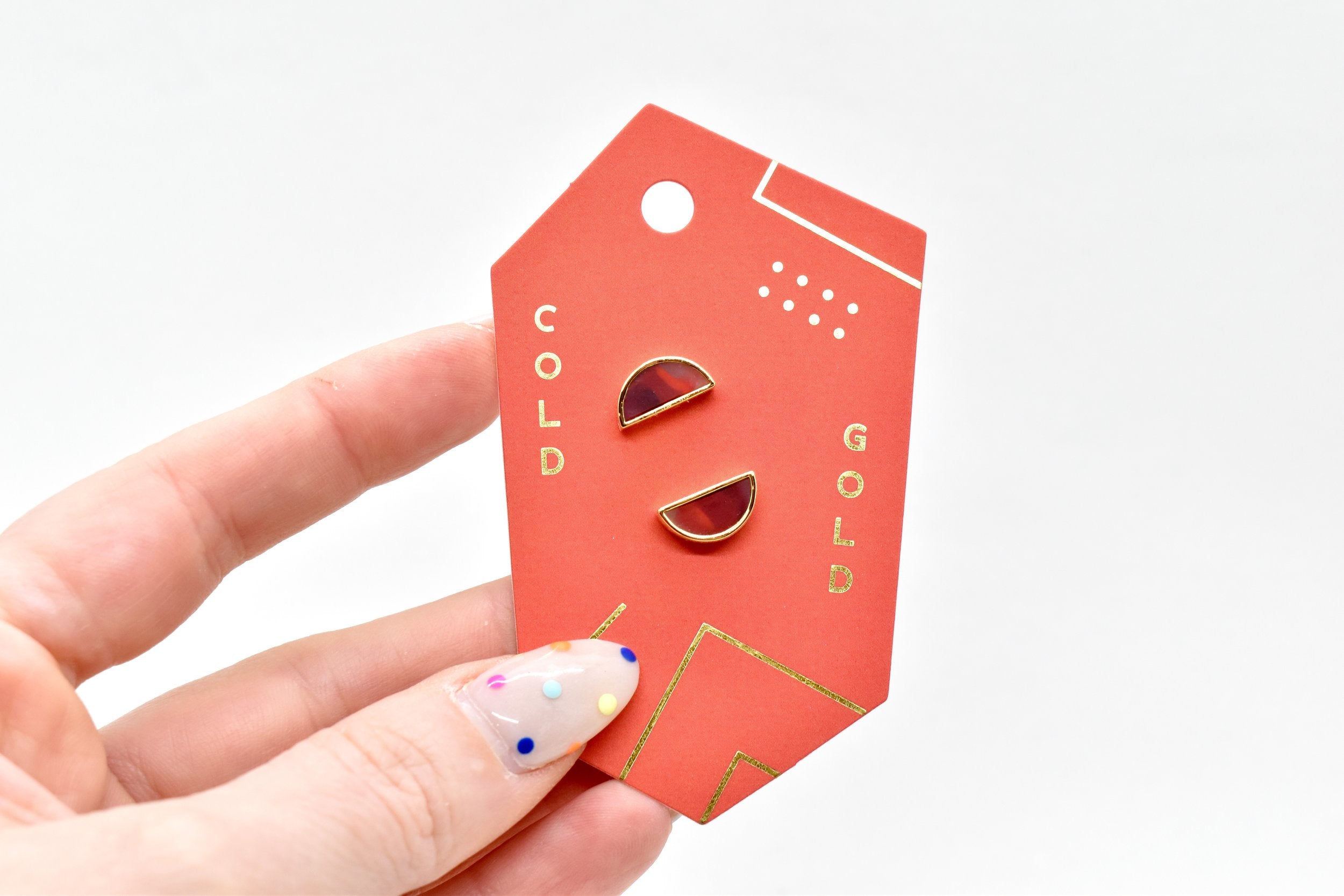 hand holding red and gold packaging card with geometric half moon stud earrings in ruby gemstone red clay