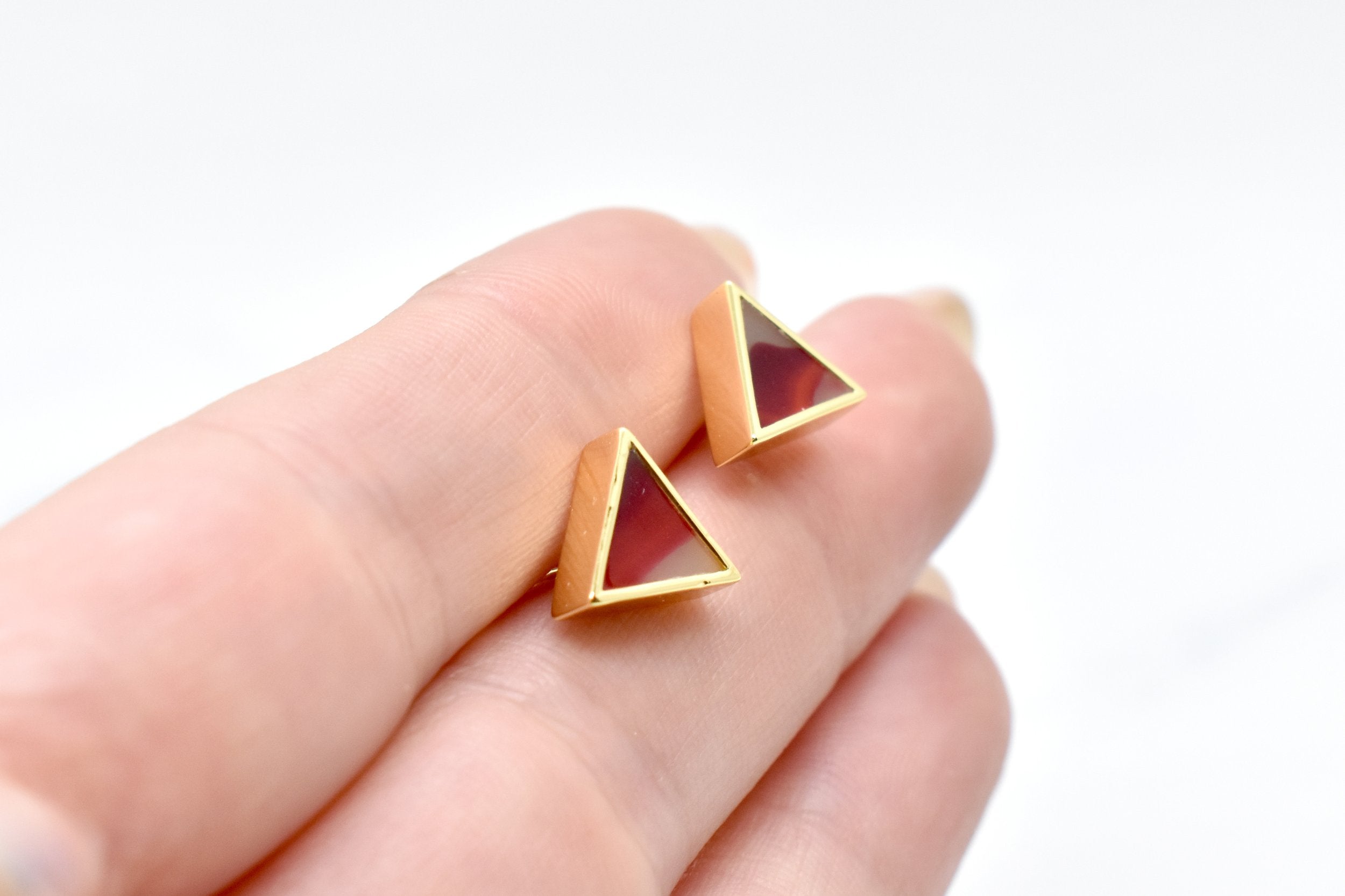 hands holding a pair of geometric triangle stud earrings in garnet red with gemstone texture clay, hand marbled to look like sapphire, a perfect gift for a July birthday