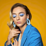 big, bold pastel blue cutout leather statement earrings styled on a blonde woman with a bold retro blue pantsuit.