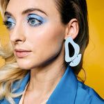 A blonde woman wears the periwinkle soft blue leather cutout statement earrings.