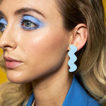 A blonde woman wears simplistic, minimal and dramatic leather cutout earrings in authentic textured baby blue leather.