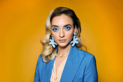 A blonde woman in a blue suit wears oversized, bold leather star shape earrings in pastel periwinkle blue.