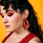 A woman wears dangling, dramatic leather cutout earrings in red. 