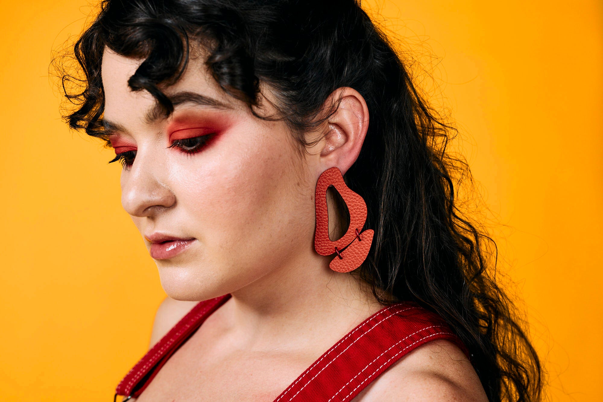 A woman wears dangling, dramatic leather cutout earrings in red. 