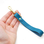 hand holding a turquoise leather keychain wristlet with gold clasp and key ring.