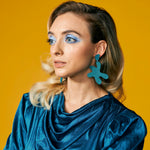 large leather cutout disco earrings in dark teal styled with a sparkling teal dress on a blonde model.