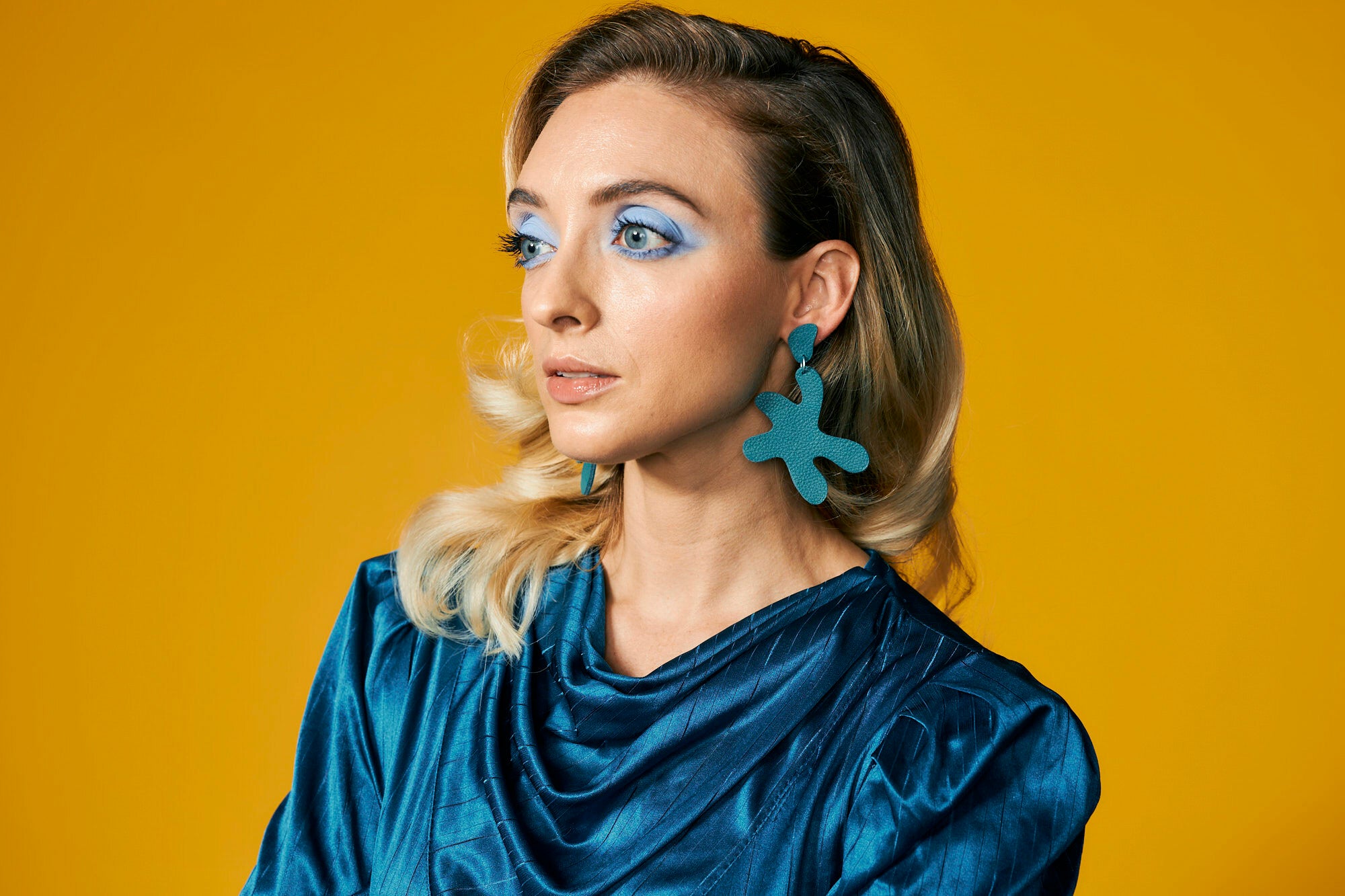 large leather cutout disco earrings in dark teal styled with a sparkling teal dress on a blonde model.