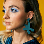 oversized turquoise leather star earrings on a model with bold blue makeup and a vintage dress.