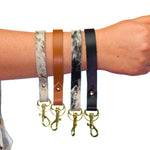 a collection of four neutral multicolored leather wristlet strap key chains hang together on an arm