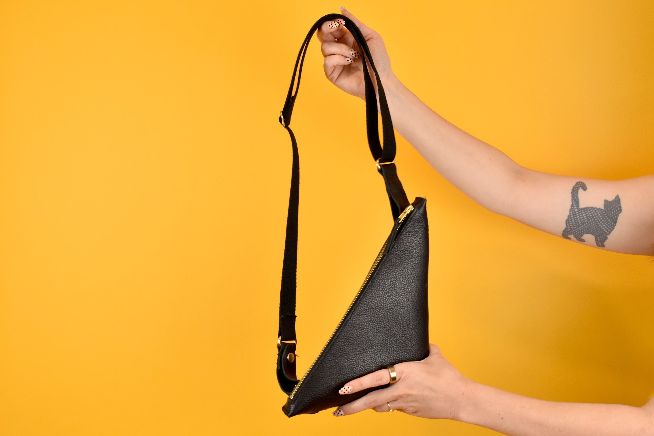 shown being held, a black triangle small leather bag, black adjustable strap for all body types