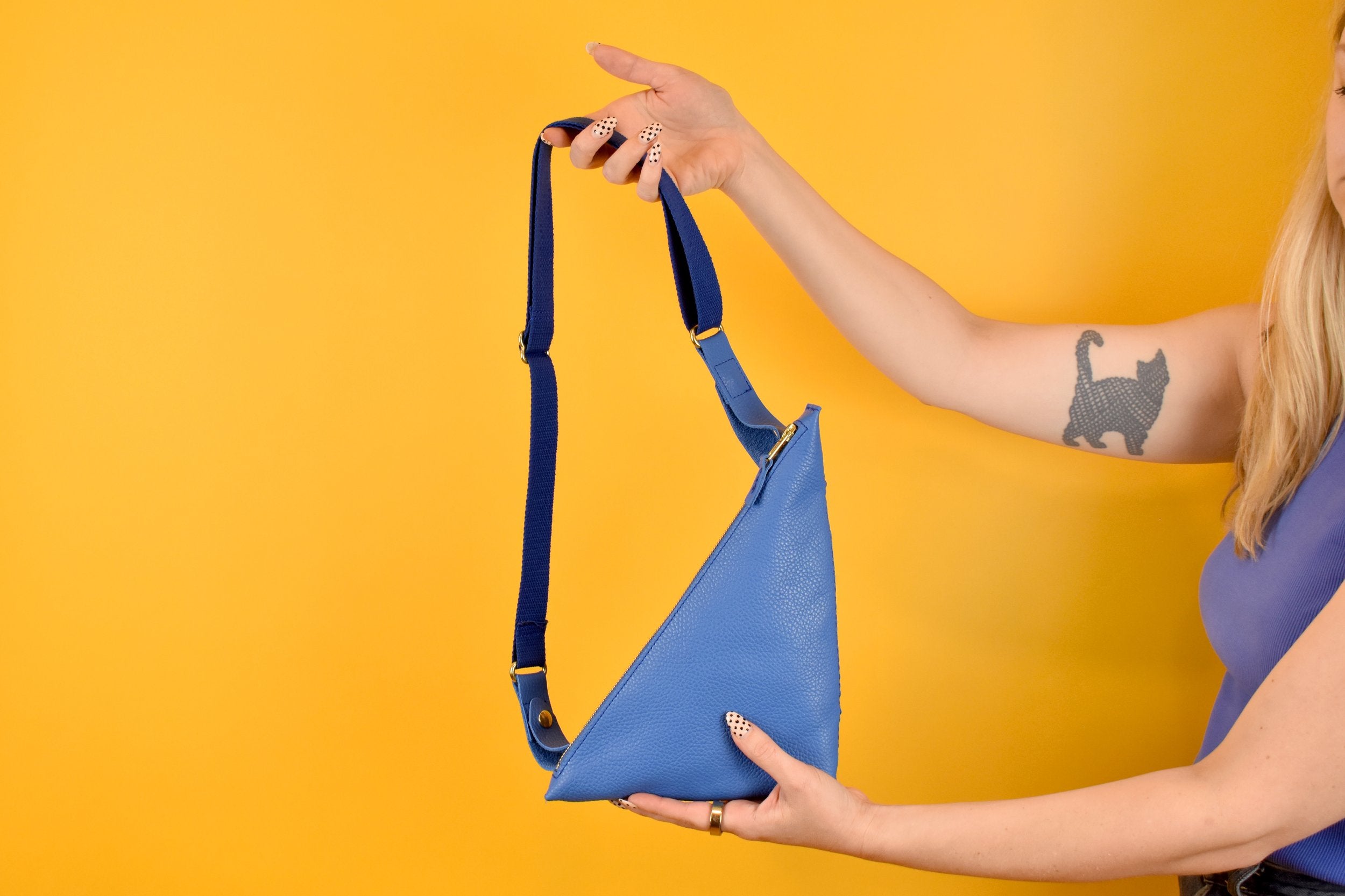 a pair of hands shown holding a matisse style sling bag purse in leather blue as a crossbody outdoor hiking bag