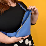person shown opening a bright blue leather purse that lays across their chest
