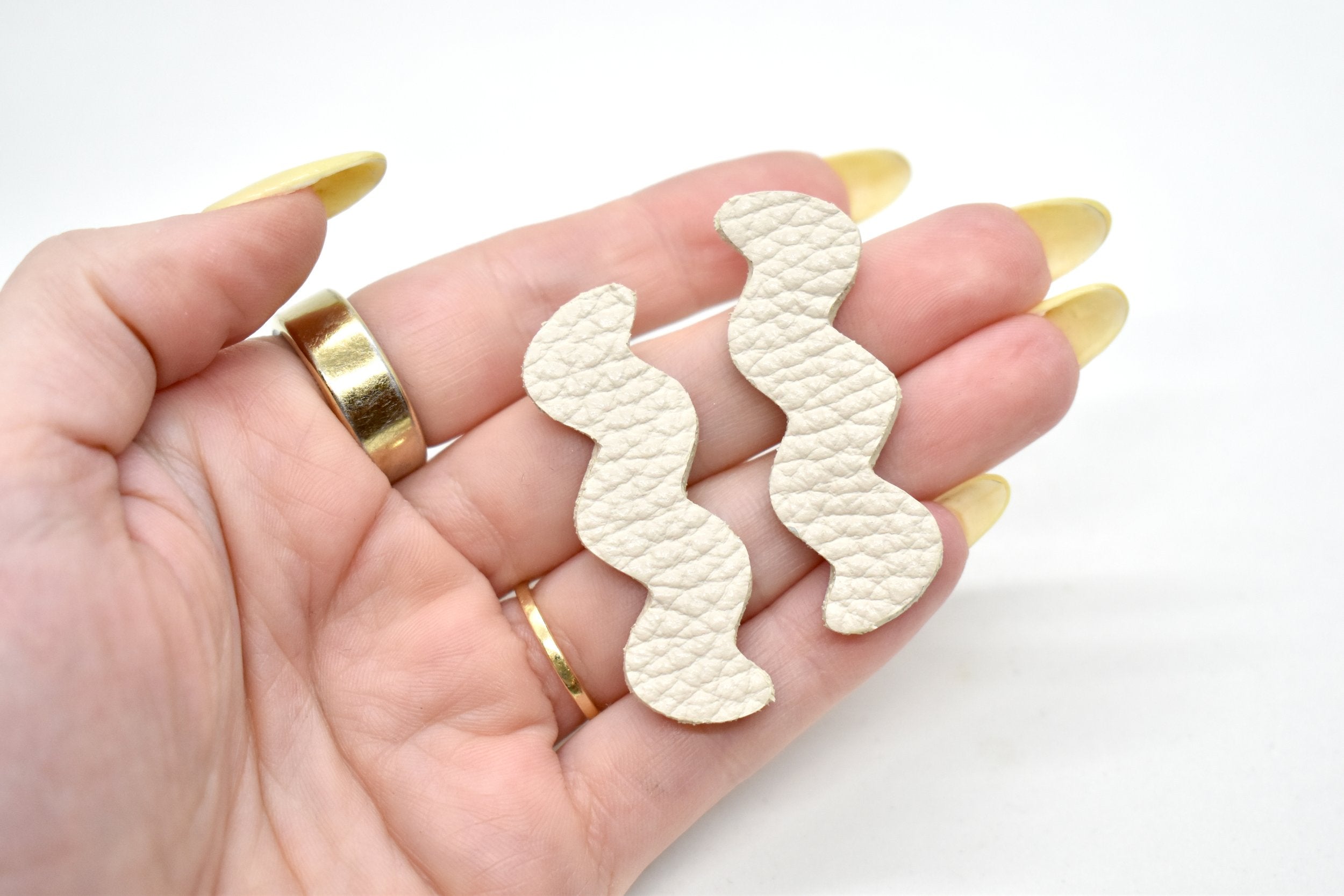a hand holds leather lightning strike cutout matisse earrings in ivory white.