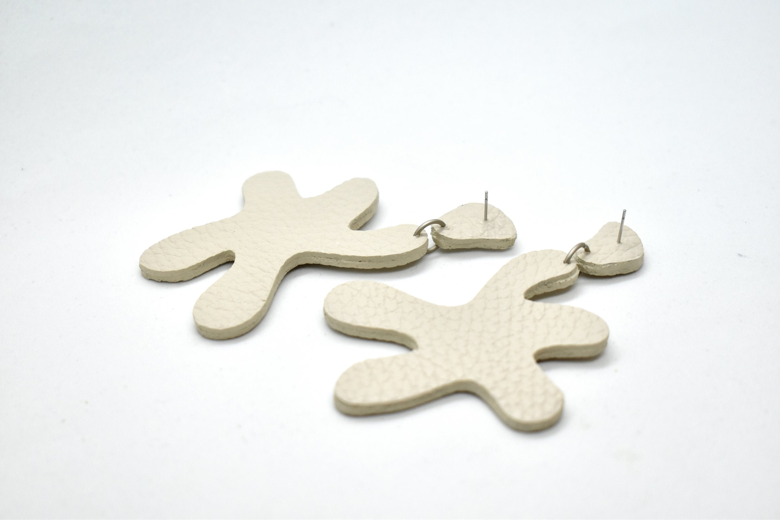 bone white leather statement earrings laying sideways to show their surgical steel posts and side profile of double sided ivory finished leather