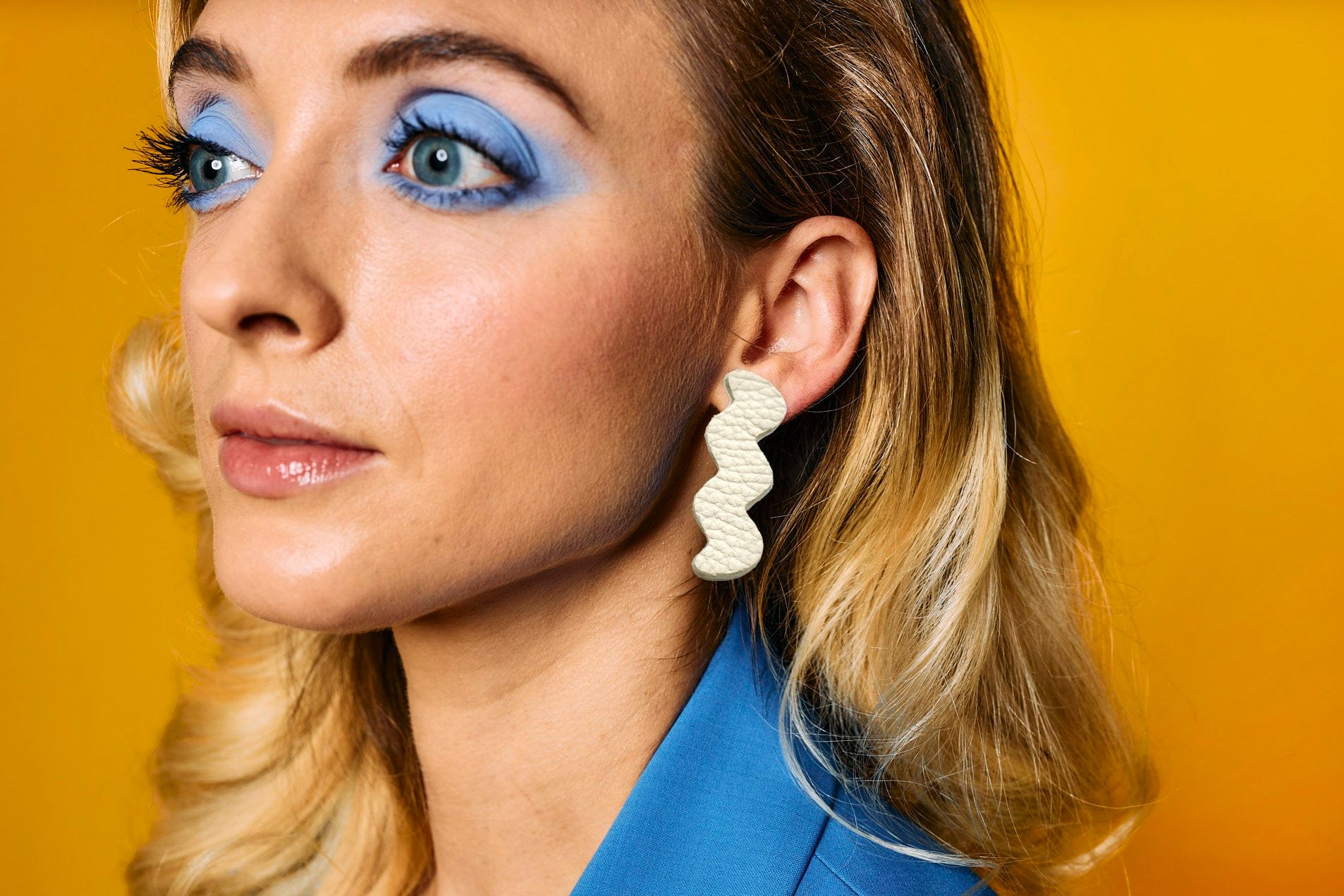 a woman wears leather cut out zig zag earrings in bone white with a blue outfit