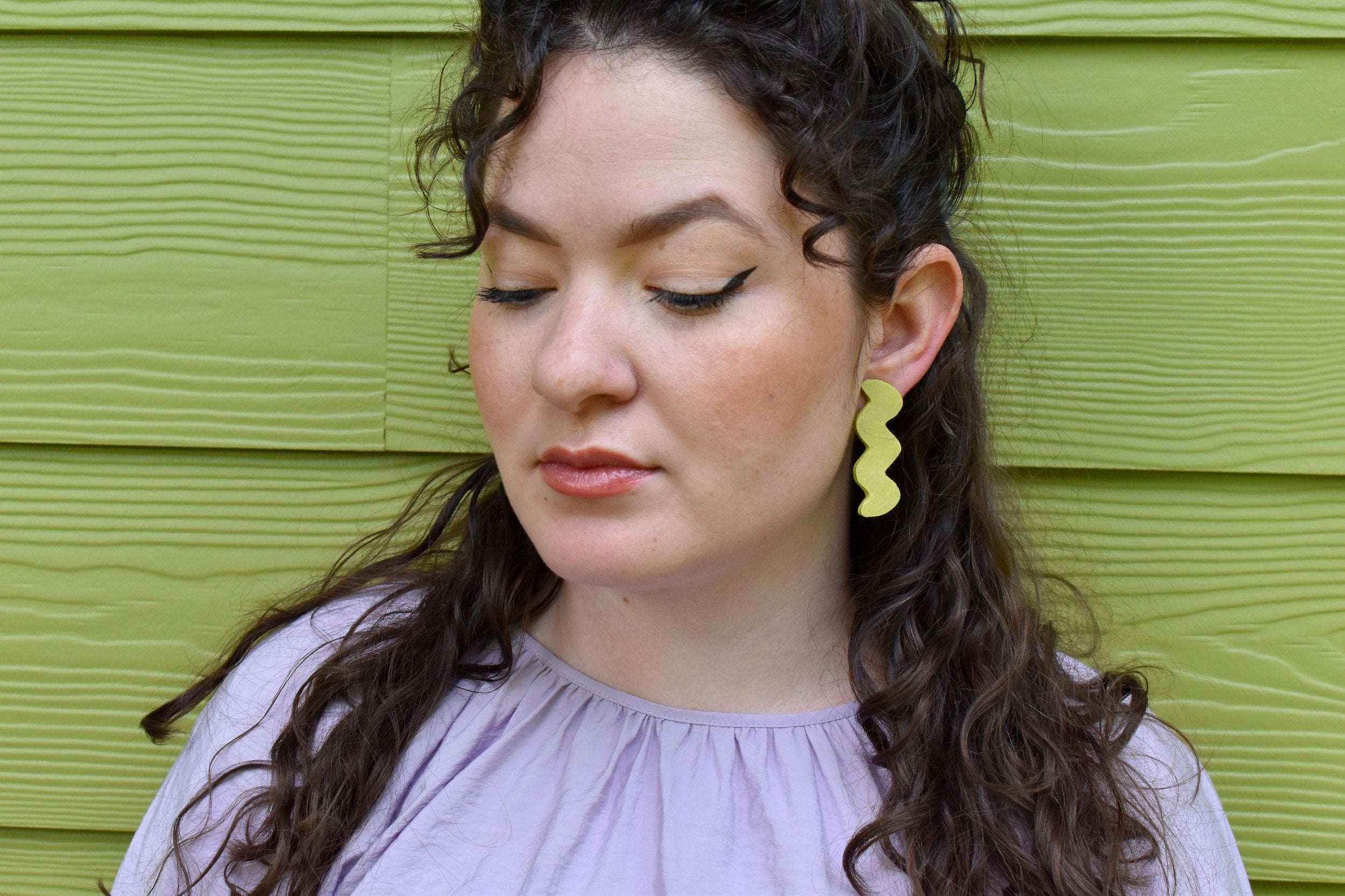 A woman wearing lightweight leather zig zag shape cutout lime earrings.