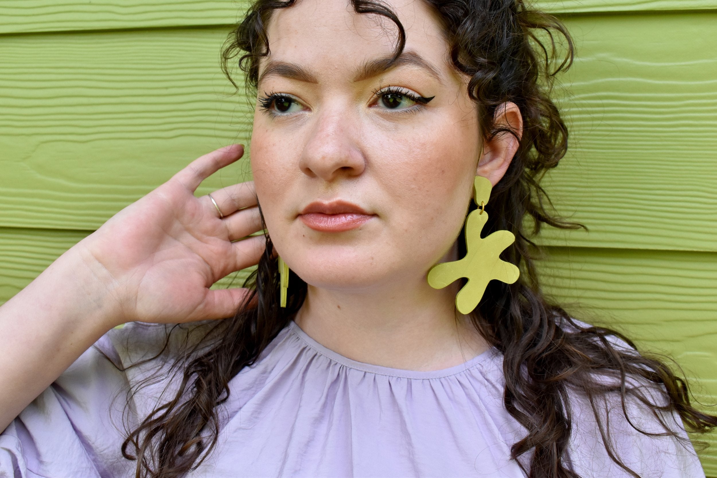 bold and modern lime green leather earrings in chartreuse on a woman with long curly dark hair.