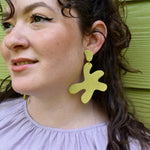 a woman styles matisse leather statement earrings in chartreuse green with a lime green background