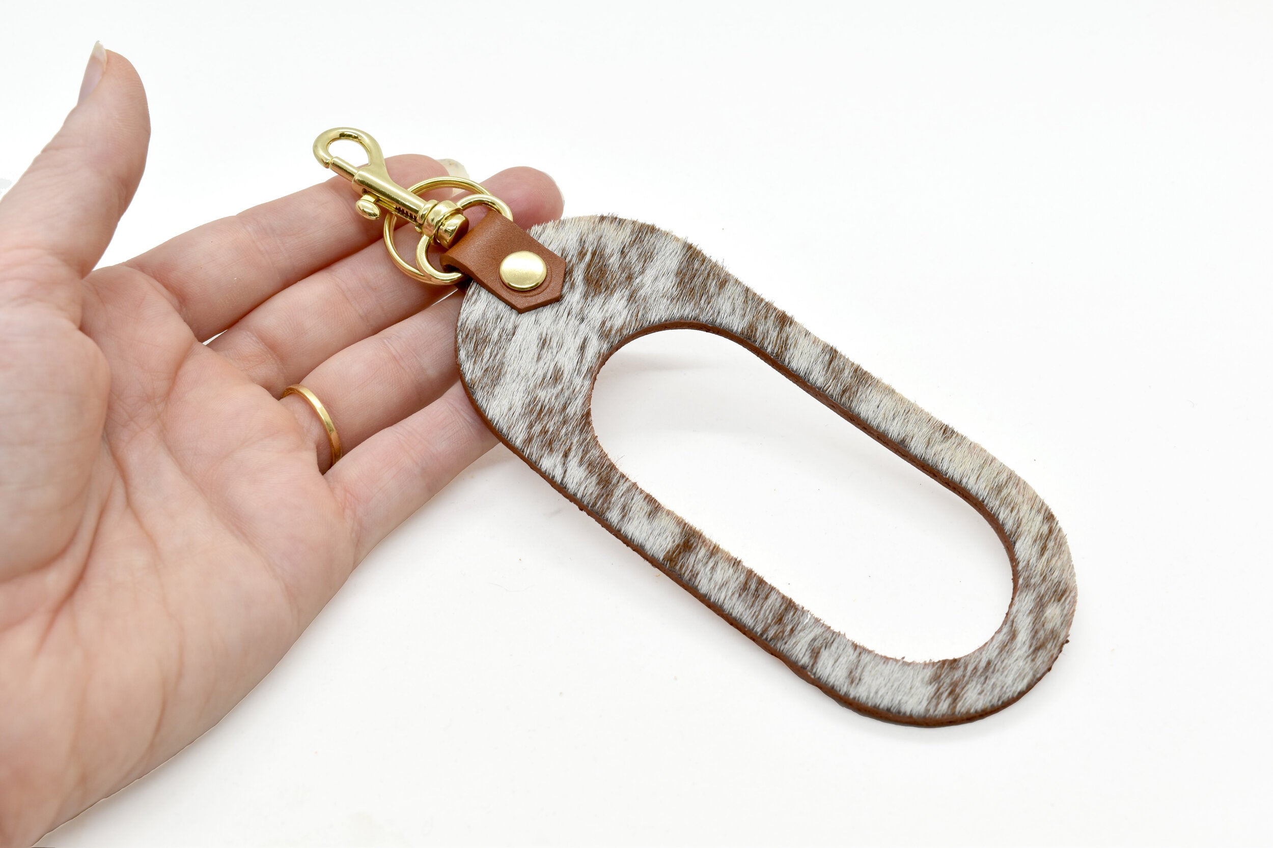 hand holding the cut out leather key chain in smooth chestnut saddle leather and chestnut brown hair on hide.