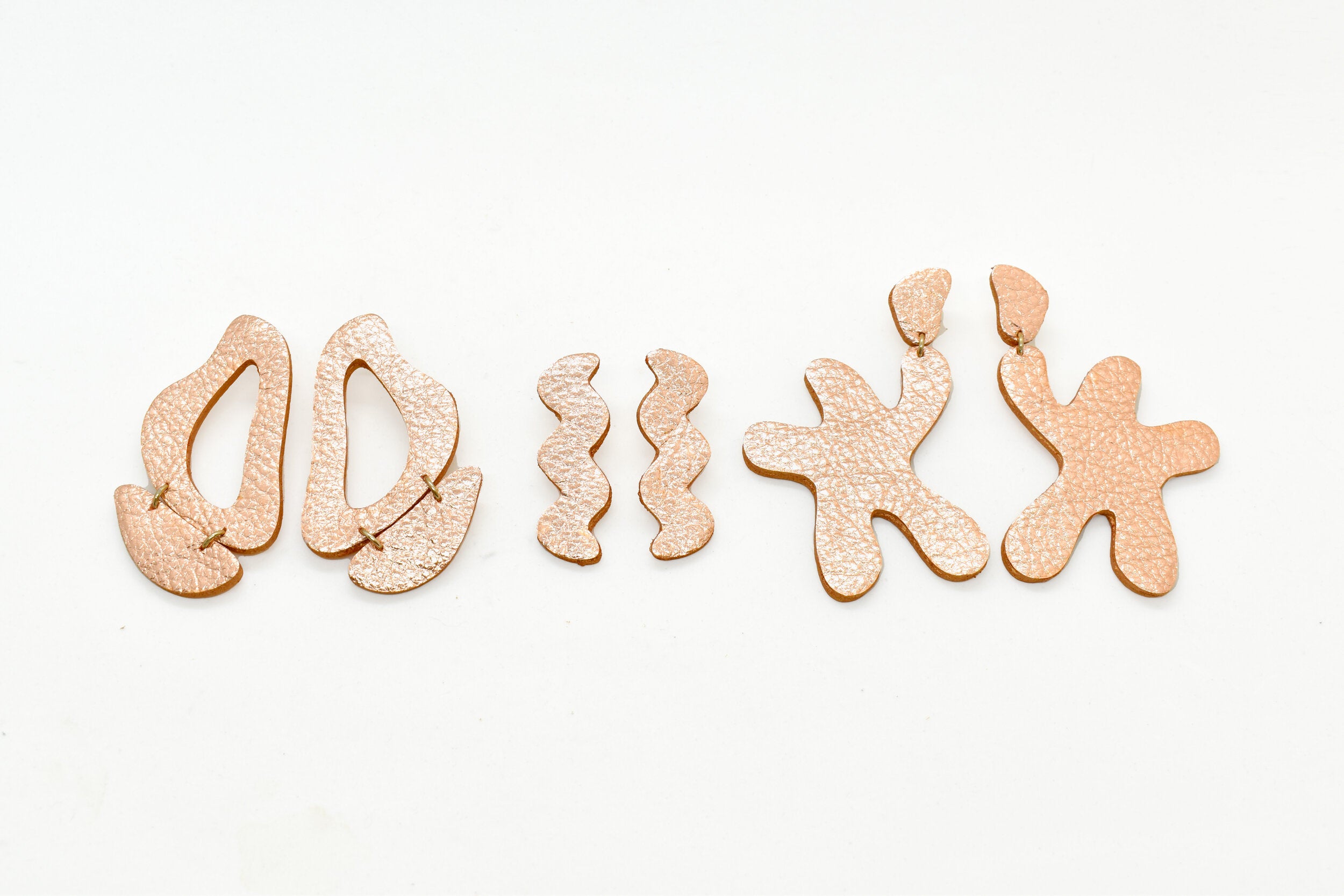 three pairs of irregular shape oversized statement earrings in metallic rose gold leather.