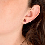 woman wearing small geometric stud earring set in 24k gold hexagon and ruby like texture gemstone