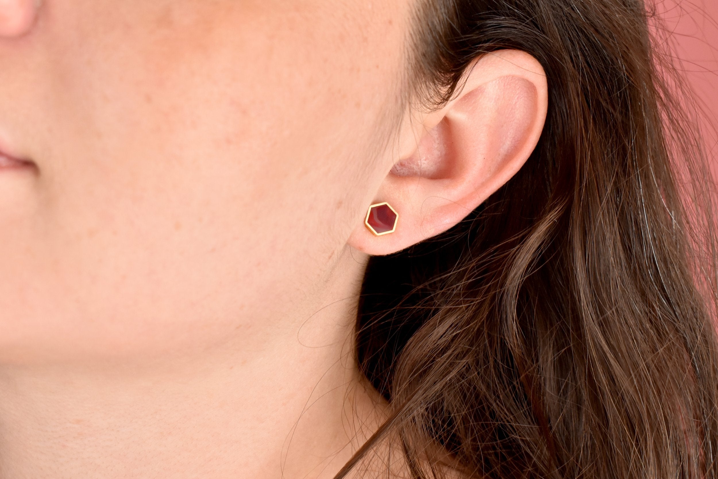woman wearing small geometric stud earring set in 24k gold hexagon and ruby like texture gemstone