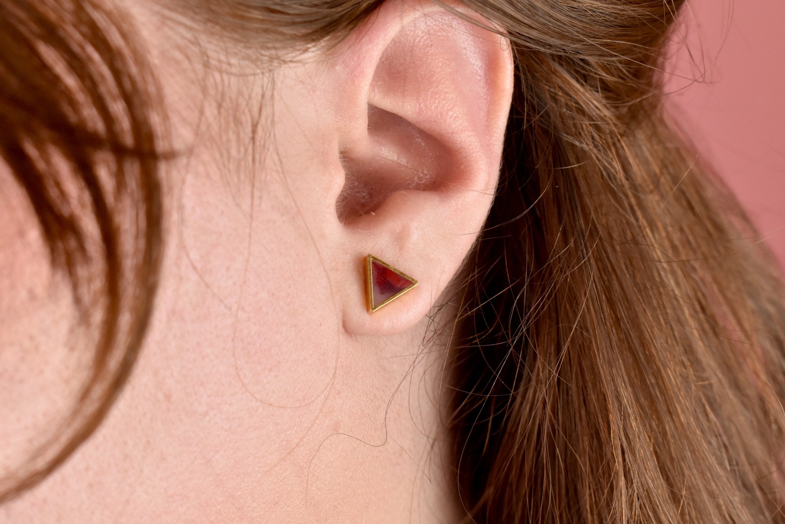 a close up photo on a model of the tiny ruby earrings in a triangle shape with 24k gold plating