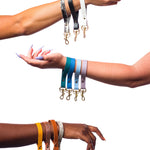 three arms in front of a white background hold multiple leather keychain wristlets in multi colors.
