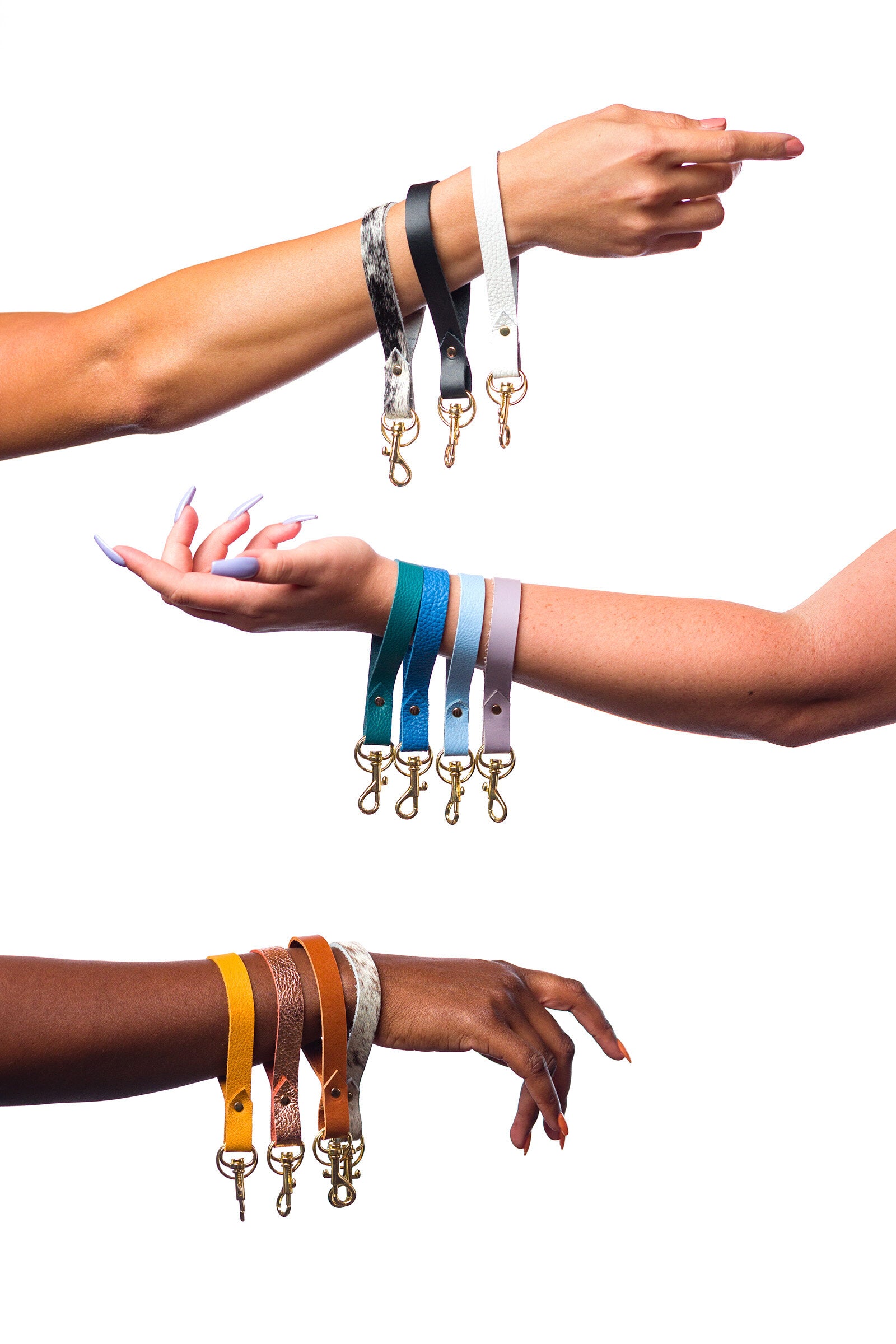 three arms in front of a white background hold multiple leather keychain wristlets in multi colors.